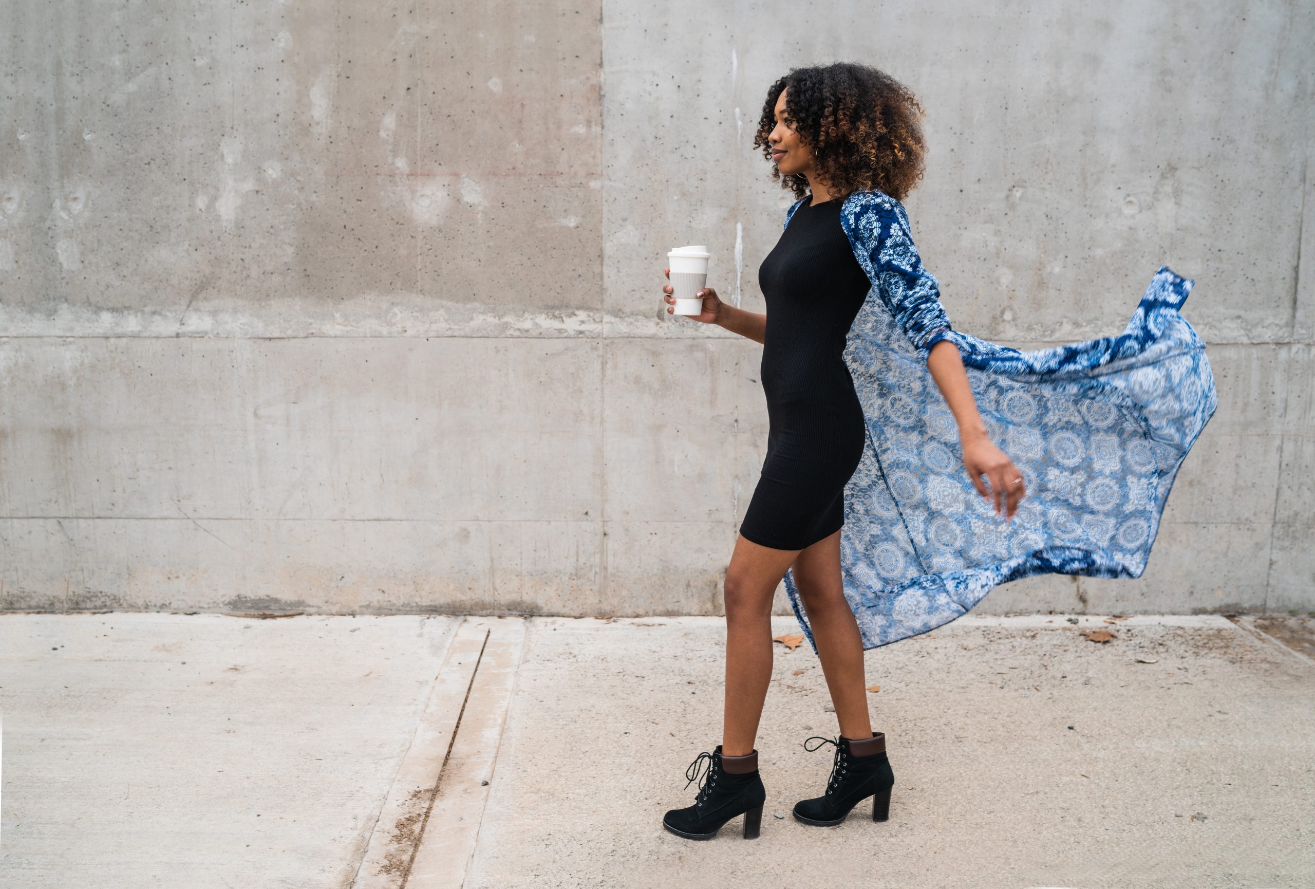 Portrait of young afro american woman walking and holding a cup of coffee. Outdoors.