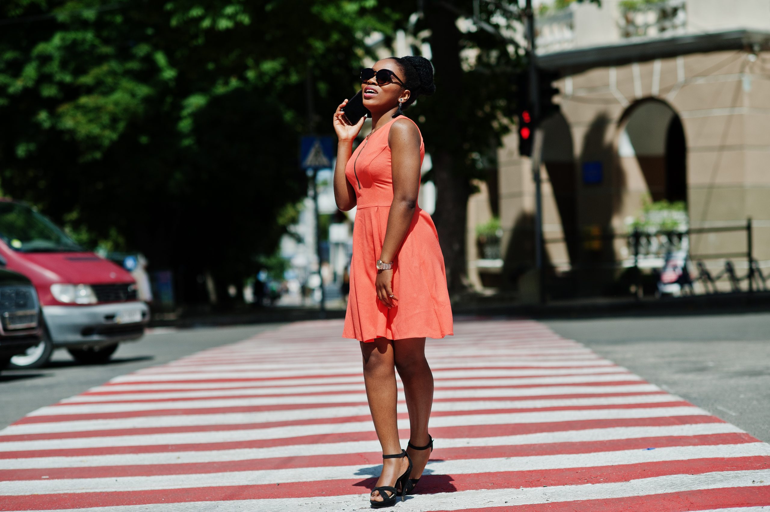 Stylish african american woman walking on crosswalk or pedestrian crossing and speaking on mobile phone.